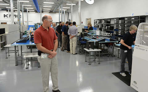 Todd Thiele inspects a production process at KMC headquarters during the  
In Touch 2012 dealer conference.  KMC's Deb Pederson feeds the wave-flow solder machine.